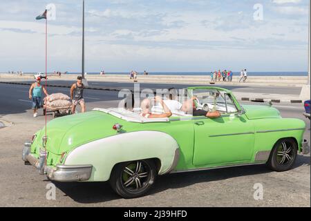 Eine Gruppe junger Leute, die mit amerikanischen Autos der 50er Jahre auf den Malecon fahren. Stockfoto