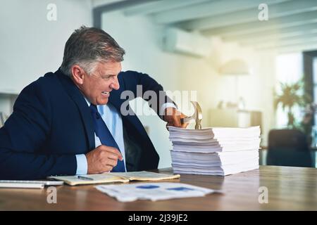 Er hat einen alternativen Ansatz für Papierkram. Aufnahme eines frustrierten Geschäftsmannes, der mit einem Hammer auf einen Haufen Papierkram schlug. Stockfoto