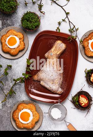Draufsicht auf hausgemachten süßen osterhasenkuchen, blumenförmige Kuchen und Nester mit Ei. Traditionelle Ostersymbole und Essen. Stockfoto