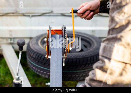 Ein Mann dreht den Windengriff auf einem Anhänger. Abschleppen und Transport von Sonderausrüstung, Be- und Entladen von Fracht. Stockfoto