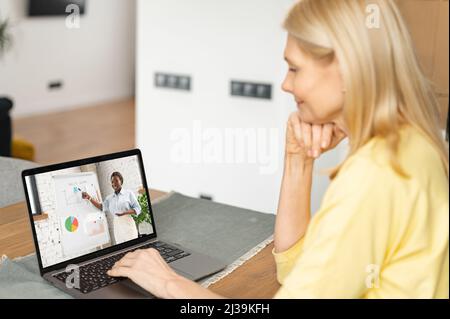 Ältere Frauen arbeiten oder studieren online. Reife Frau sieht sich Online-Kurse an. Konzept von Fernstudien, Online-Lernen, Webinaren. Rückansicht Stockfoto