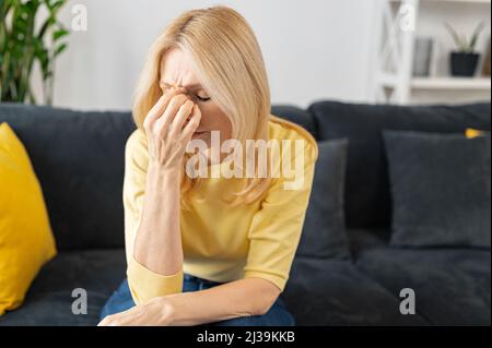 Besorgte Frau, die die Stirn mit der Hand zu Hause auf dem Sofa hält, verzweifelte Frau, die Probleme hat oder etwas wichtiges vergessen hat, Kopfschmerzen empfindet Stockfoto