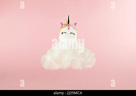 Ostereinhorn-Ei fliegt auf Wolke auf pastellrosa Hintergrund. Frohe ostern Banner. Inspiration für Aktivitäten für Kinder. Grußkarte oder Poster. Speicherplatz kopieren für Stockfoto