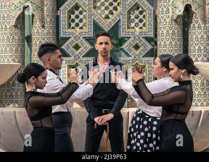 Gruppe von Schülern, die in Flamenco gekleidet sind, tanzen zu zweit vor ihrem Lehrer und blicken auf die Kamera Stockfoto