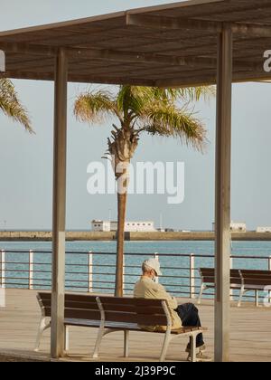 Alter Mann, der allein auf einer Bank mit Blick auf das Meer sitzt Stockfoto