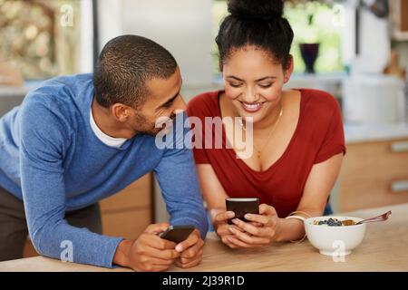 Intelligente Technologien in ihrer Ehe zum Einsatz bringen. Aufnahme eines glücklichen jungen Paares, das zu Hause sein Smartphone zusammen benutzt. Stockfoto