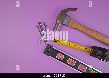 Flatlay von Hammer, Nägel, Maßband und Level isoliert auf einem Lavendel lila Hintergrund Stockfoto