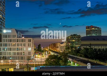 Halbmond in wolkenverhangendem Himmel bei Nacht über dem La Defense District mit Gebäuden Stockfoto