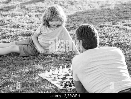 Vater und Sohn spielen Schach auf Gras. Vatertag. Glückliche Familie. Stockfoto