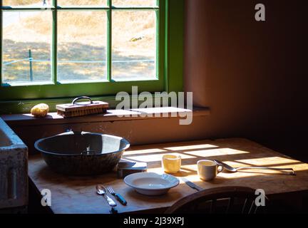 Alte Zeiten Bauernhaus Interieur eines alten Landhauses Küche. Ländliche Wohnküche mit abgenutztem Holztisch und Rührschüssel, Löffel, Teller. Selektiver Fokus Stockfoto