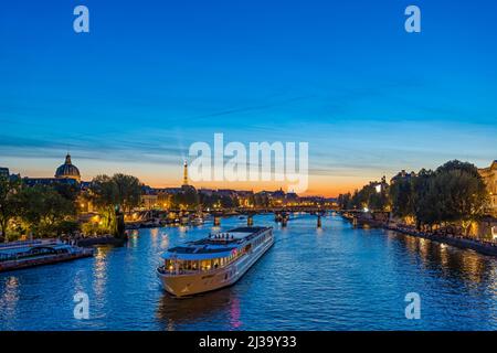 Riesige Boote fahren bei Sonnenuntergang in der Dämmerung über die seine in Paris mit Eiffelturm Stockfoto
