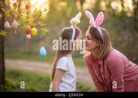 Schöne und glückliche Mutter und Tochter in Hasenohren schmücken den Baum mit ostereiern. Glückliche Familie feiert ostern. Stockfoto