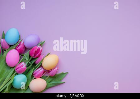 Ostereier und Tulpenblumen auf rosa Hintergrund. Osterkarte mit verzierten Eiern und Tulpenblumen. Christliche Ostereier auf einem rosa Hintergrund mit Stockfoto