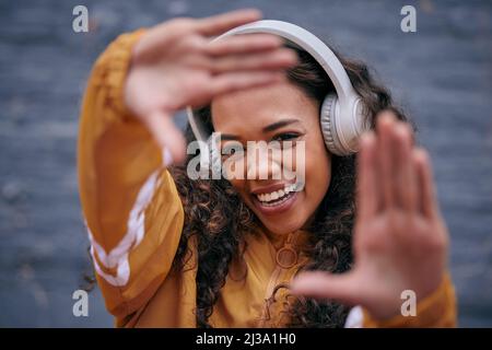 Gute Musik macht mich glücklich. Kurze Aufnahme einer schönen jungen Frau, die Kopfhörer trägt, während sie draußen steht. Stockfoto