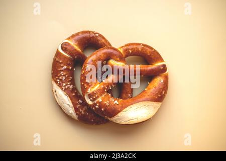 Zwei frisch gebackene Brezeln aus der Nähe, isoliert auf beigefarbenem Hintergrund. Stockfoto