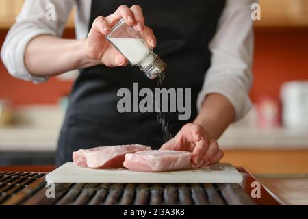 Der Küchenchef bereitet frische Schweinefleisch Steaks in der Küche, Salz das Fleisch der Speisekarte, Hausmannskost. Kulinarische Rezepte. Restaurant-Menü. Stockfoto