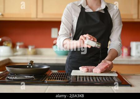 Der Küchenchef bereitet frische Schweinefleisch Steaks in der Küche, Salz das Fleisch der Speisekarte, Hausmannskost. Kulinarische Rezepte. Restaurant-Menü. Stockfoto