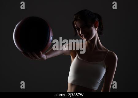 Teenager Mädchen mit Basketball. Seitlich beleuchtetes Studioporträt vor dunklem Hintergrund. Stockfoto