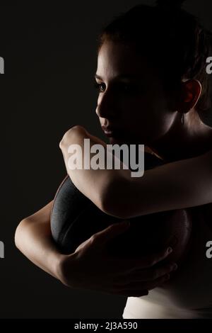 Teenager Mädchen mit Basketball. Seitlich beleuchtetes Studioporträt vor dunklem Hintergrund. Stockfoto