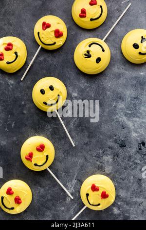 Mehrere Emoticon-Merengue-Cookies vor dunklem Hintergrund verstreut. Stockfoto