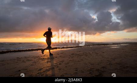 Silhouette Mann läuft am Strand von Takapuna bei Sonnenaufgang, Rangitoto Island im Hintergrund, Auckland. Stockfoto