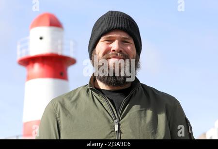 05. April 2022, Mecklenburg-Vorpommern, Warnemünde: Monchi (Jan Gorkow), Sänger der Punkband feine Sahne Fischfilet, vor dem DOCK INN Hostel. Der 34-Jährige hat ein Buch mit dem Titel 'Niemals satt' ('über den Hunger nach Leben und 182 Kilo auf der Skala') geschrieben, das am 7. April 2022 bei Kiepenheuer & Witsch veröffentlicht wird. Gleichzeitig startet er eine Lesetour über 17 Stationen. Foto: Bernd Wüstneck/dpa Stockfoto