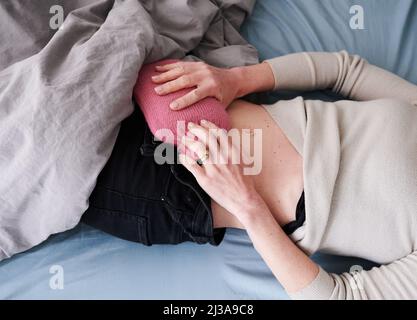 Berlin, Deutschland. 30. März 2022. ABBILDUNG - Eine Frau hält eine Wärmflasche an ihren Unterbauch, während sie im Bett liegt. (Posed scene) viele Betroffene der Bauchkrankheit Endometriose leiden im Alltag unter schweren Symptomen und damit verbundenen Einschränkungen. (To dpa: 'Mysterium Endometriose - Wenn die Zeit zur Qual wird') Credit: Annette Riedl/dpa/Alamy Live News Stockfoto