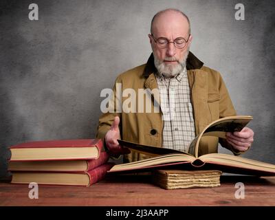Zwangloses Studioporträt eines bärtigen älteren Mannes, der alte Bücher liest und durchstöbert Stockfoto