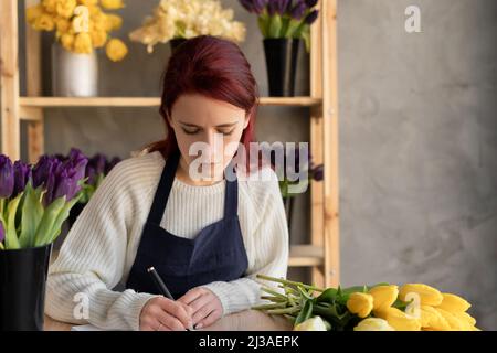 Eine weibliche Geschäftsinhaberin schrieb einen Auftrag für einen Blumenstrauß in ein Notizbuch auf. Europäisches Blumengeschäft Konzept. Stockfoto