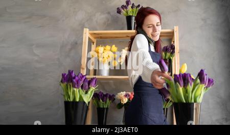 Ein kleines Geschäft. Eine Frau Floristin in einem Blumenladen in der Nähe einer Vitrine mit Tulpen in einer Schürze sammelt einen Strauß Tulpenblumen nimmt eine Bestellung per Telefon Stockfoto