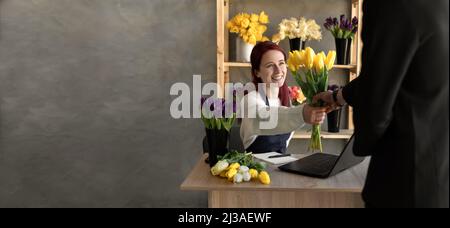 Ein junger Mann kauft für den Urlaub eines Mädchens in einem gemütlichen Blumenladen einen schönen Blumenstrauß aus Tulpenblumen. Floristik und Herstellung von Blumensträußen in einem Blumenladen Stockfoto