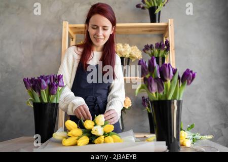 Junge schöne Frau Floristin in einer Arbeitsschürze sammelt einen Strauß Tulpen. Stockfoto