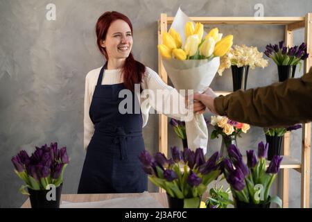 Ein junger Mann kauft einen schönen Blumenstrauß für den Urlaub eines Mädchens in einem gemütlichen Blumenladen. Floristik und Herstellung von Blumensträußen in einem Blumenladen. Stockfoto