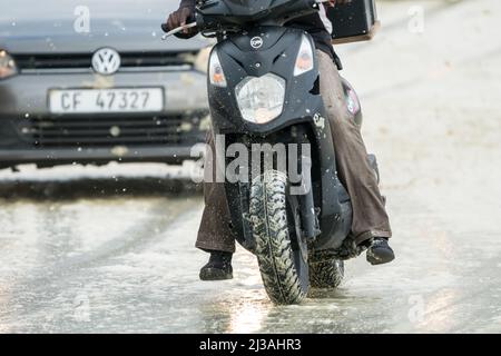 Roller oder Motorrad verlieren während eines Sturms bei Winterfahrkonzepten oder Straßenverkehrssicherheit auf einer rutschigen, nassen Straße vor einem Auto die Kontrolle Stockfoto