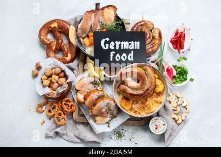 Traditionelle deutsche Küche, Schweinshaxe-Schinken-Hock. Bier, Brezeln und verschiedene bayerische Spezialitäten auf Holzbrett, weißer Backgroun, Draufsicht. Stockfoto