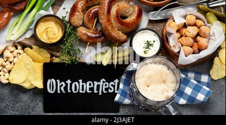 Oktoberfest Tischkonzept mit gegrillten Schweinswürsten, Brezelteig, Kartoffeln, Salat, Snacks, Saucen, Bier auf dunklem Hintergrund, Draufsicht. Stockfoto