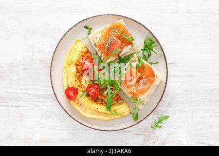 Omelette oder Omelette, frischer Rucola- und Tomatensalat und Toast mit Butter und gesalzenem Lachs. Frühstück. Draufsicht Stockfoto