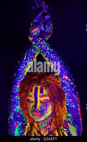 Neongöttin. Ausgeschnittene Aufnahme einer jungen Frau, die mit Neonfarbe auf ihrem Gesicht posiert. Stockfoto