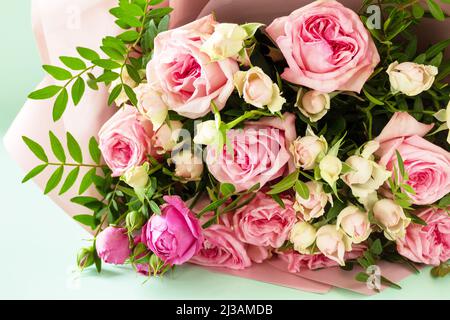 Muttertag, Frauentag oder Geburtstagskarte. Schönes Bouquet von blühenden zarten rosa Rosen und Frühlingsgrün auf grünem Hintergrund. Stockfoto