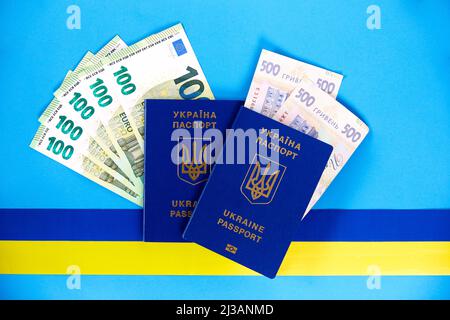 Zwei biometrische Pässe von ukrainischen Bürgern und Euro-Banknoten und ukrainischer Griwna auf blauem Hintergrund mit einem gelben und blauen Band. Der Koncep Stockfoto