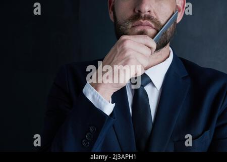 In meinem Geschäft lohnt es sich, poliert auszusehen. Aufnahme eines nicht identifizierbaren Geschäftsmannes, der seinen Bart mit einem Kamm vor einem dunklen Hintergrund sticht. Stockfoto