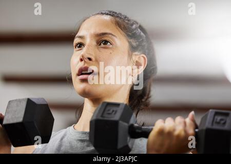 Geist über Materie. Low-Angle-Aufnahme einer sportlichen jungen Frau, die mit Kurzhanteln im Fitnessstudio trainiert. Stockfoto