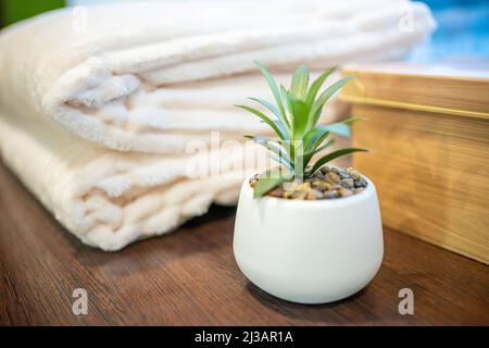 Weiß gestapelte Badetücher und Blume im Topf auf einem hölzernen Hintergrund Stockfoto