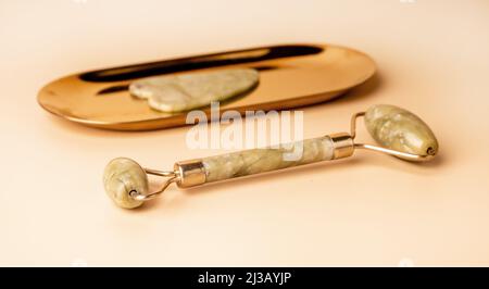 Gua Sha Massagegeräte. Abstreifer und Walze auf goldenem Ständer und beigem Hintergrund. Instrumente zur Akupunkturtherapie, Triggerpunktbehandlung. Hochwertige Fotos Stockfoto