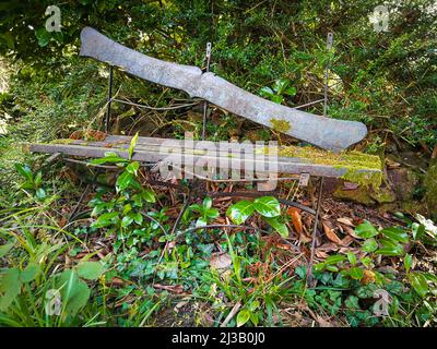 Alte, reparaturbedürftige Holzbank, die in einem verlassenen Garten fast überwuchert ist Stockfoto