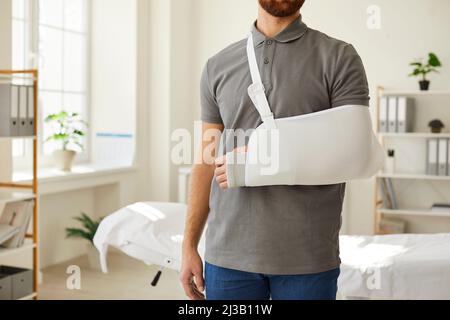 Unbekannter Mann, der am gebrochenen Arm eine Armbinde trägt, steht im medizinischen Büro. Stockfoto