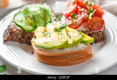 Feta-Sandwiches mit Avocado, Kirschtomaten und Gurken aus der Nähe. Bruschetta mit Weichkäse und Gemüse. Stockfoto