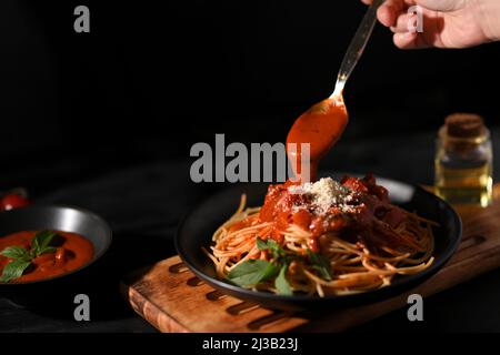Weibliche Hand garnieren und bereiten italienische Pasta Spaghetti mit Tomatensauce. Italienisches Speisekonzept Stockfoto