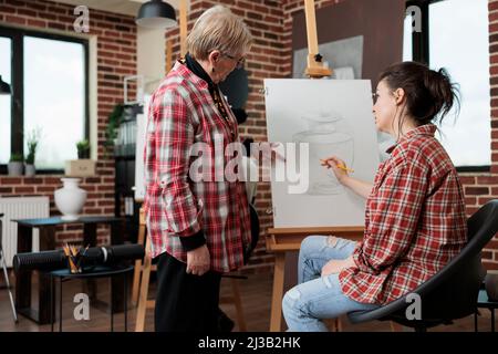 Leitender Kunstlehrer, der jungen Schülern während des Kreativitätsunterrichts im Schulstudio Grafiktechnik zeigt. Malerin Frau Zeichnung Vase Skizze mit Bleistift skizzieren arbeiten in persönlichen Wachstum Stockfoto