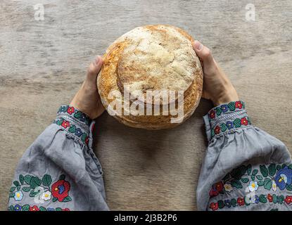 Eine Frau in ukrainischer Nationaltracht hält frisches Brot aus dem Ofen. Sauerteig hausgemachtes Brot. Stockfoto